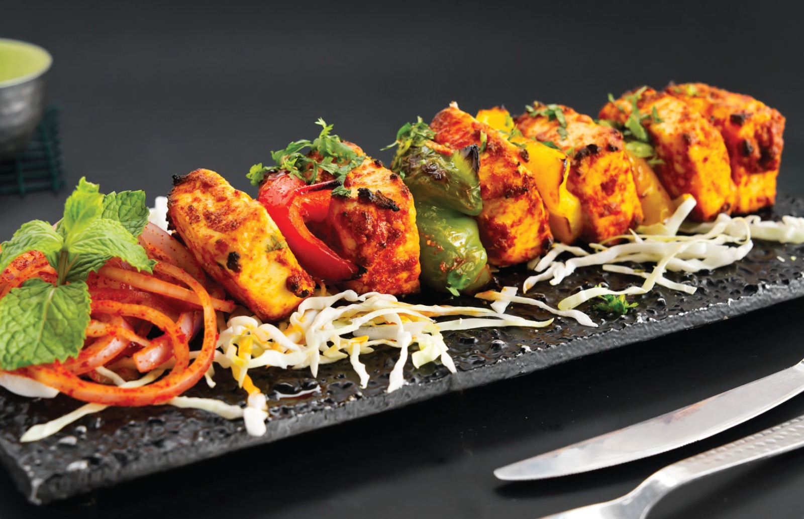 paneer kebab on a long black plate garnished with mint