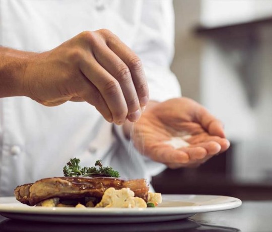 chef plating a meal, garnishing with salt