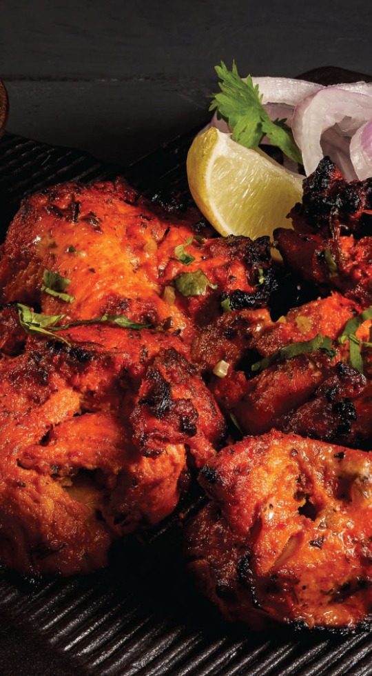 Tasty Indian food with a south Asian twist, from Dhinchak Croydon chicken tikka on a black plate served with lemon and onions